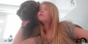 A young girl with blonde hair leaning affectionately against a large, calm Sarplaninac dog.